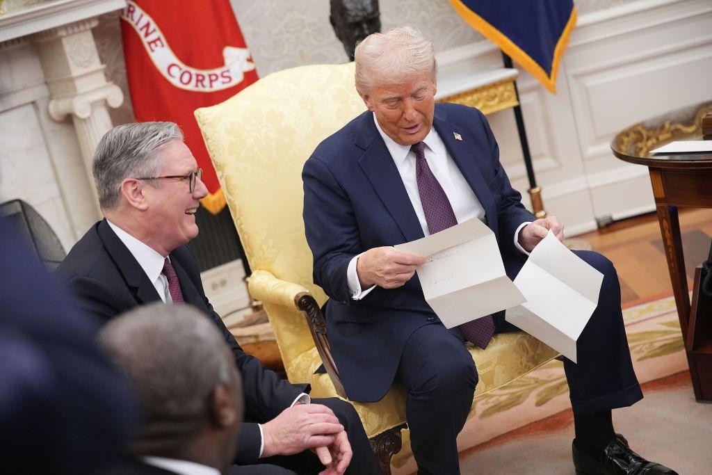 Sir Keir Starmer and Donald Trump seated. Mr Trump is reading a letter from the King. Both men are relaxed and smiling. 