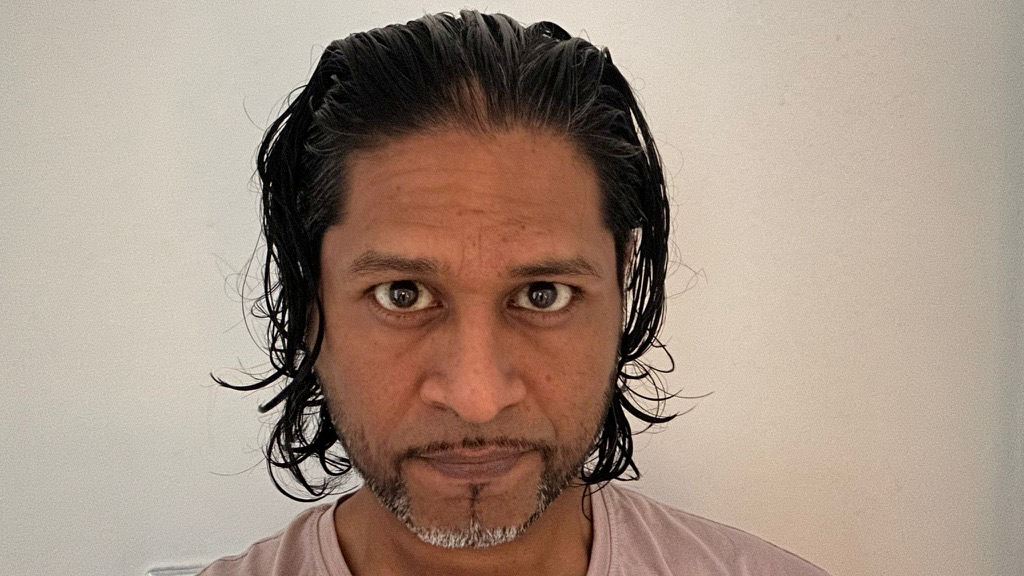 Shah has his hair slicked back and is wearing a peach coloured t-shirt