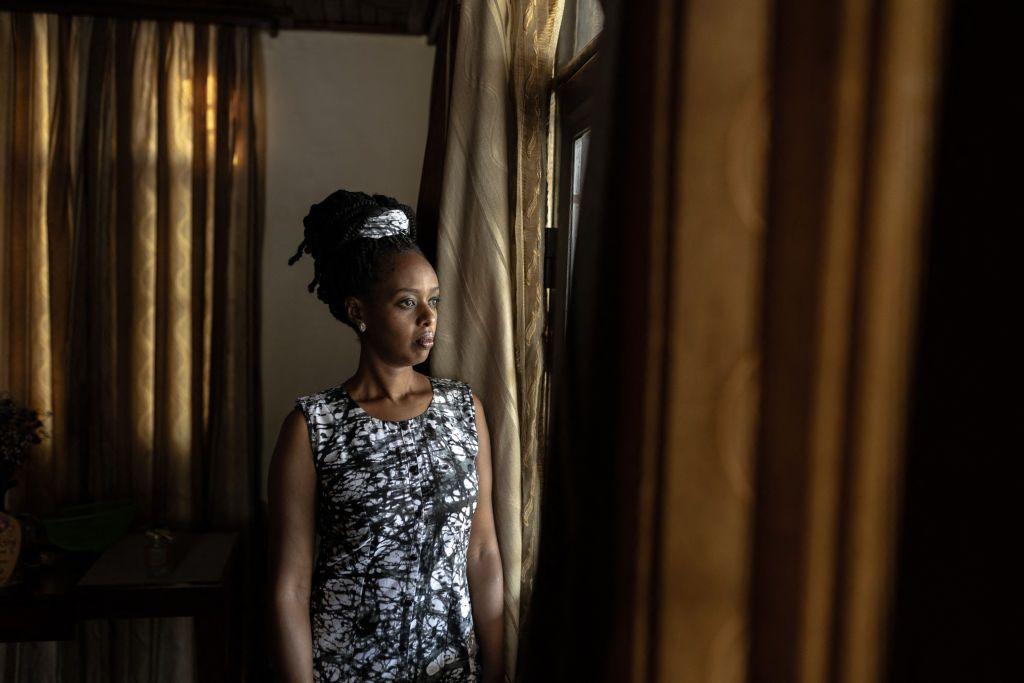 A woman standing in a sombre room looks out a window.