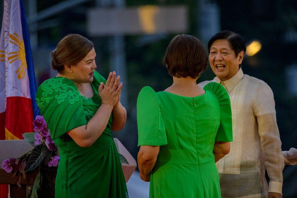 A laughing Sara Duterte, wearing a birght green dress, speaks with President-elect Ferdinand "Bongbong" Marcos Jr, who is wearing a white shirt and trousers, after taking her oath as the next vice-president on June 19, 2022. 