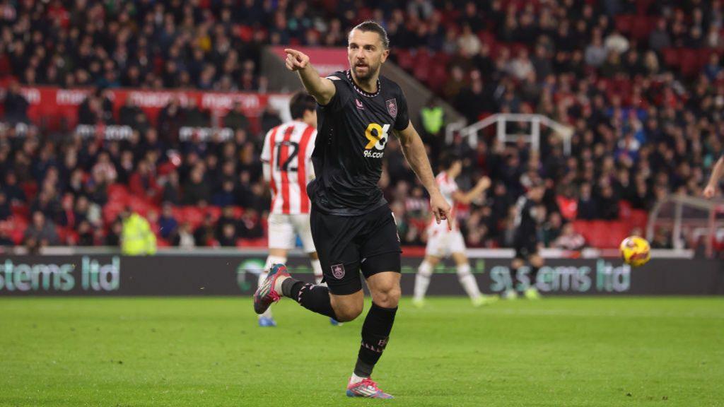 footballer wearing black points into the distance in celebration on grass pitch