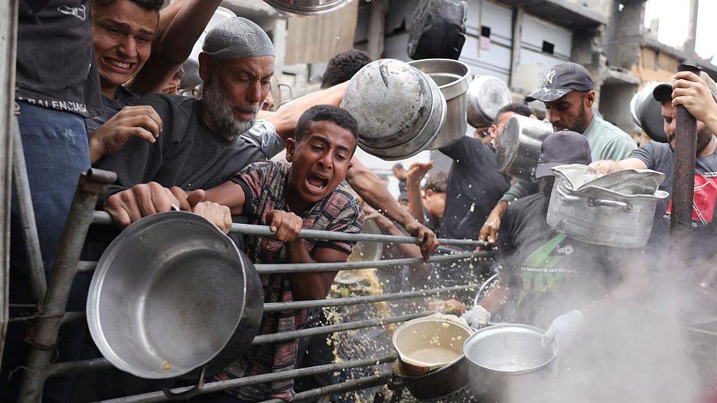 People hold pots and cry out and jostle as they try to get food in Gaza