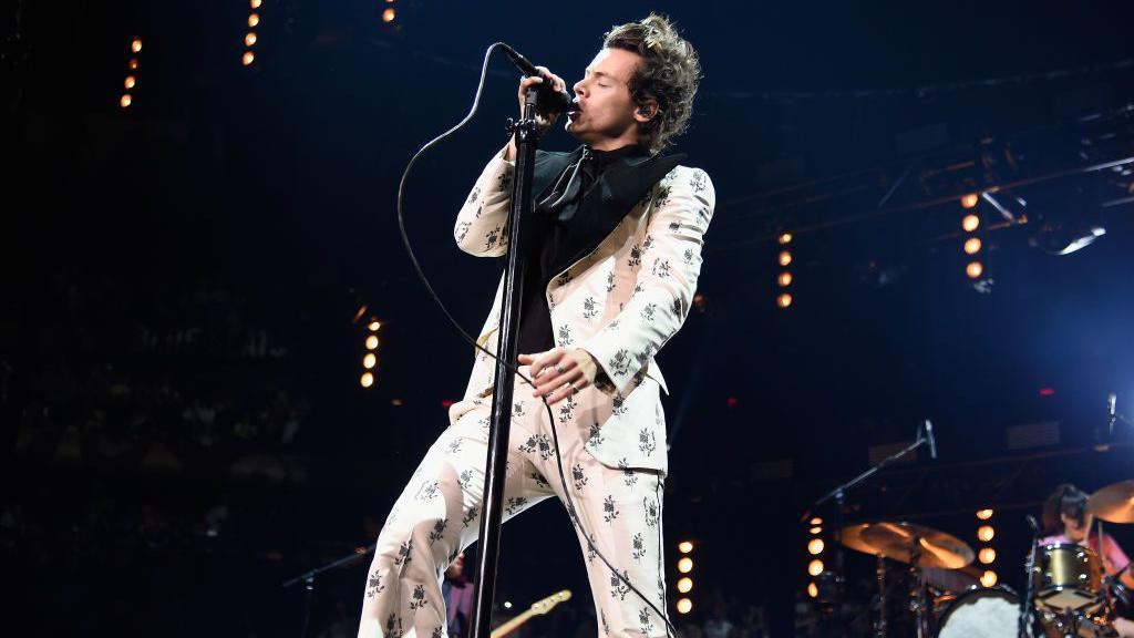 Harry Styles performing on stage in a white suit