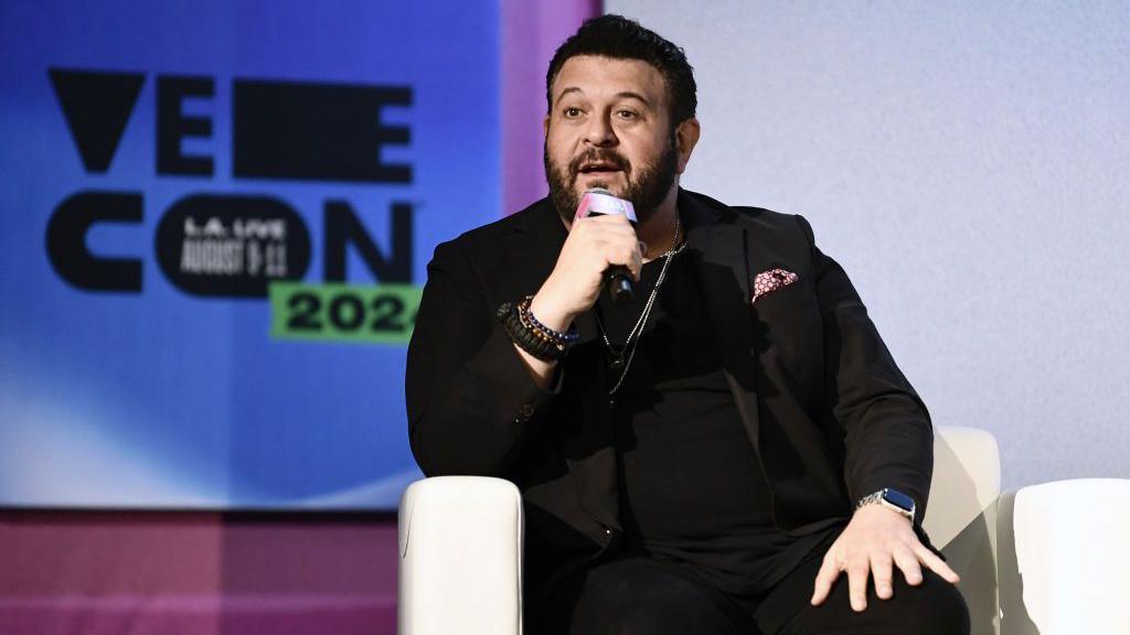 Adam Richman in a black suit jacket and t-shirt speaking during VeeCon 2024