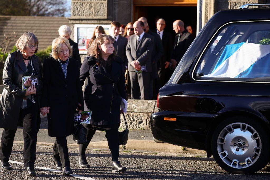 Moira Salmond pictured at her husband Alex Salmond's funeral in Strichen, Aberdeenshire. She is one of three female mourners walking behind the cae. Other mourners can be seen in the background and the casket is covered with a Saltire.