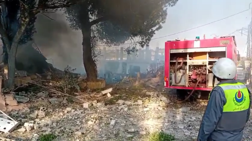 An emergency worker stands by as smoke is seen rising from a bombed home