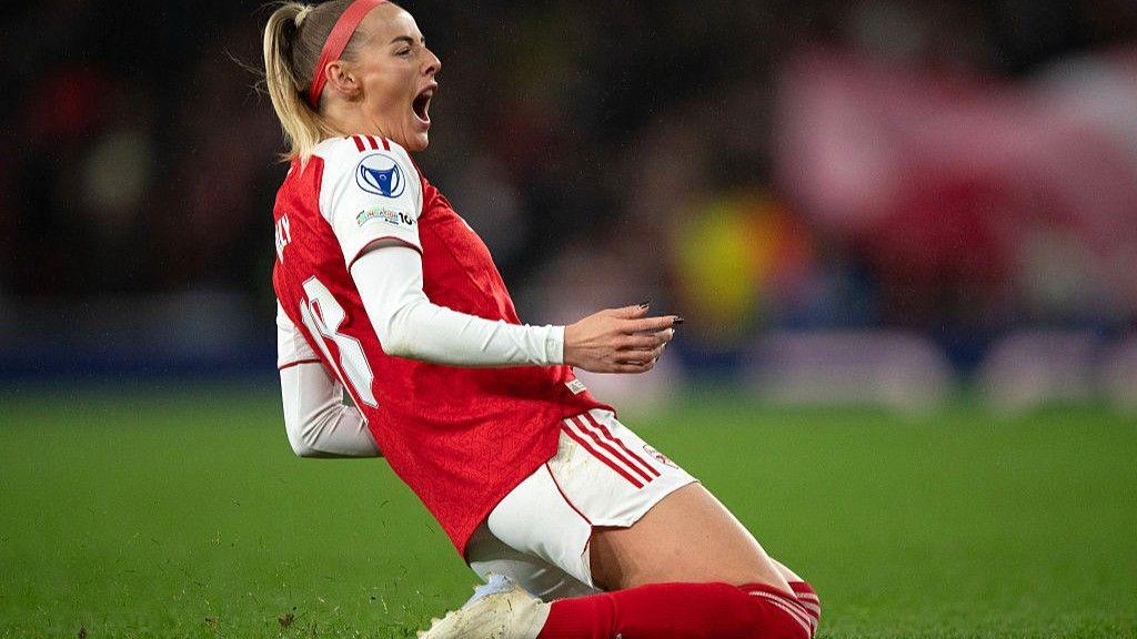 Chloe Kelly slides on her knees in celebration while wearing Arsenal's red and white kit and a red headband