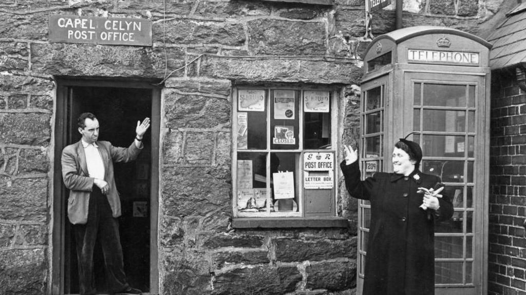Mr Jones Parry, the postmaster, outside his post office at Capel Celyn in December 1956, waving to a customer