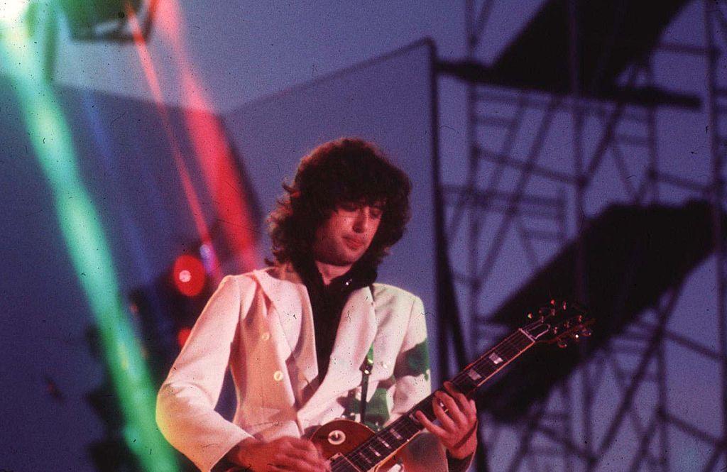 Jimmy White on stage in Tampa, Florida in1974. He has long hair and is wearing a white jacket while playing a guitar.