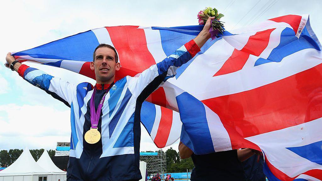 Etienne Stott holding the Union Flag in his arms, after winning a gold medal