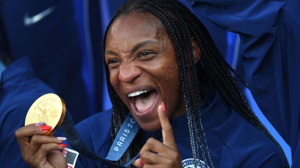 Crystal Dunn smiles while holding an Olympic gold medal