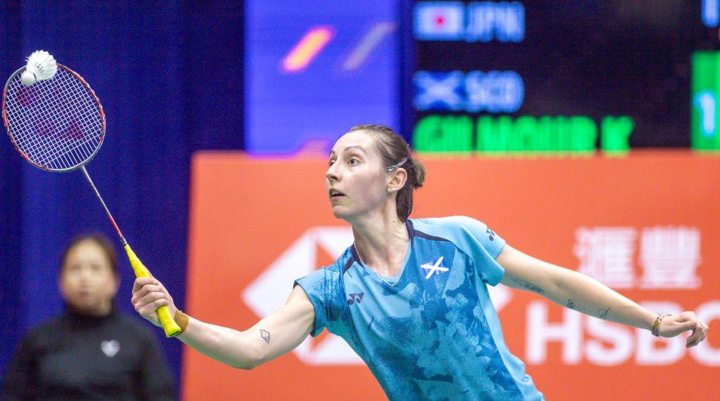 Woman in blue Scotland t-shirt, holding badminton racquet and hitting a shuttlecock. She is clearly playing in a high level competition. 