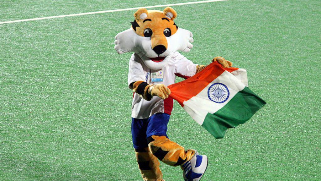 a tiger mascot on a green pitch holding an Indian flag