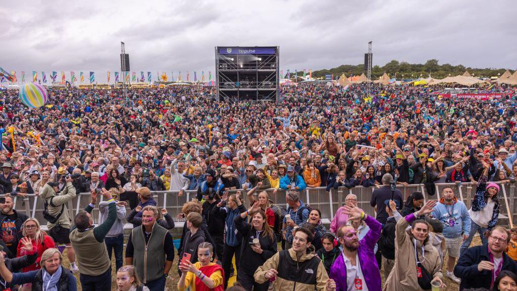 Thousands of people waiting for acts at CarFest in Hampshire last year, with flags bordered the back of the site.