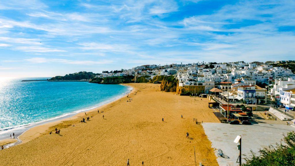 A view of the Albufeira coastline in Portugal. People enjoy the sand beach which is overlooked by white buildings.