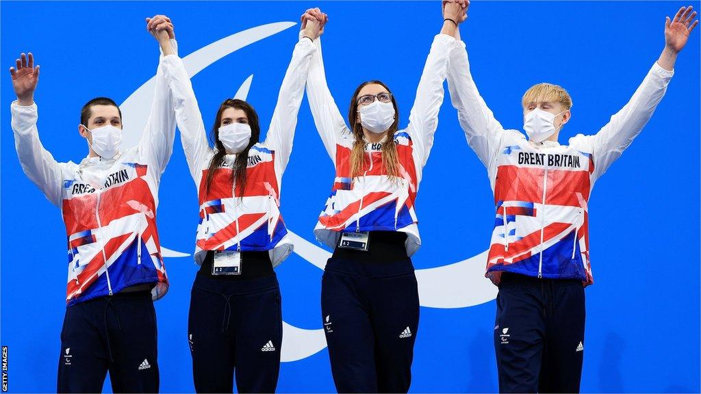 Gold medallists Reece Dunn, Bethany Firth, Jessica-Jane Applegate and Jordan Catchpole of Great Britain stand on the medal podium and lift their arms up in celebration after winning the mixed 4x100m freestyle relay at the Tokyo Paralympics