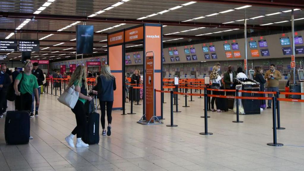 Passengers with suitcase wander London Luton Airport near non-busy check-in desks