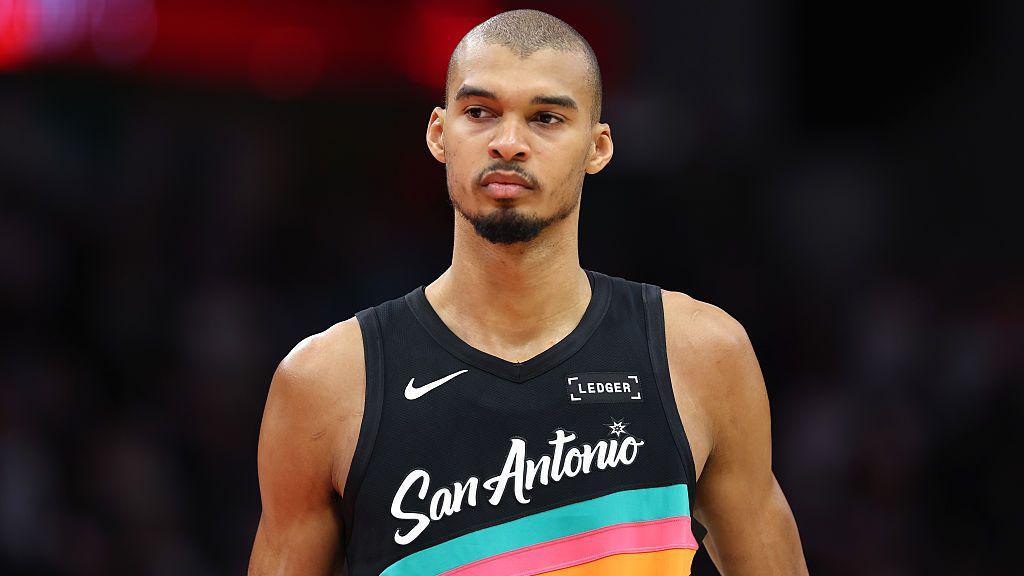 Victor Wembanyama wearing a vest that is black with blue, pink and orange stripes and the words San Antonio across the front