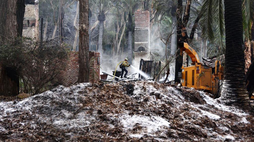 Firefighters spray white retardant on buildings that have burned on Wednesday