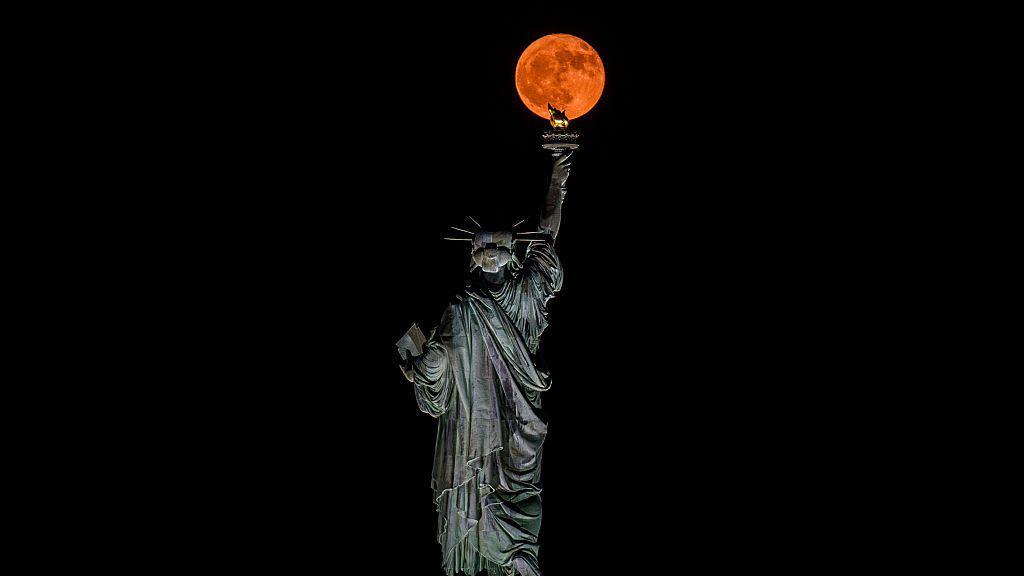 Strawberry Moon above the Statue of Liberty in New York City.