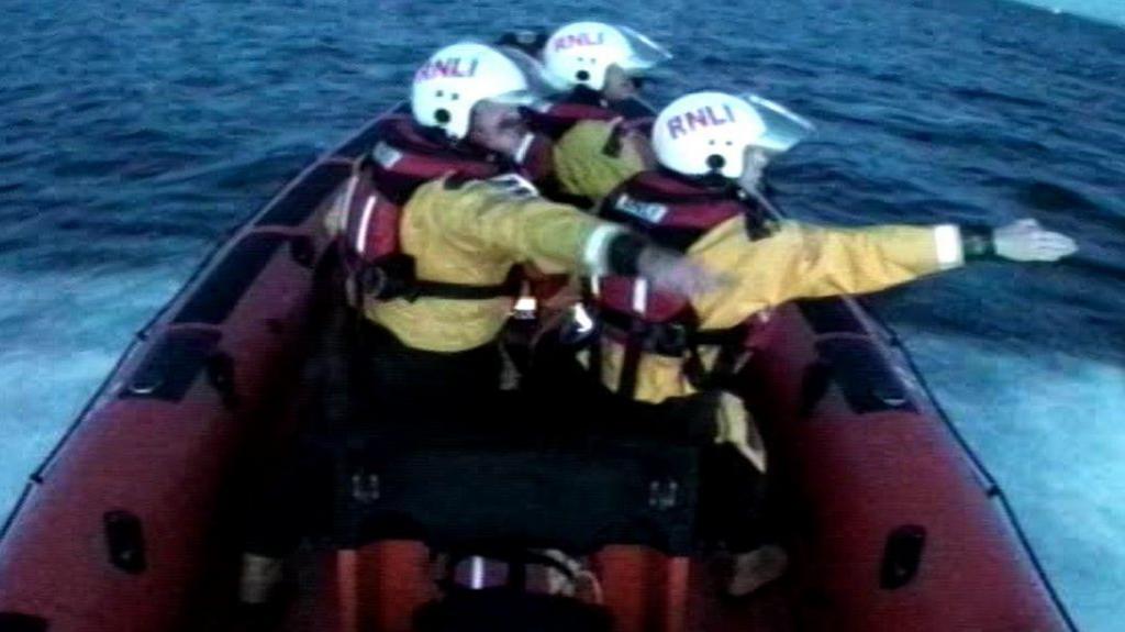 Three lifeboat crew point to the sound of noise