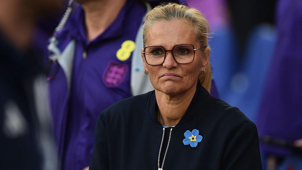 A frowning Sarina Wiegman in dark top and yellow and blue broach