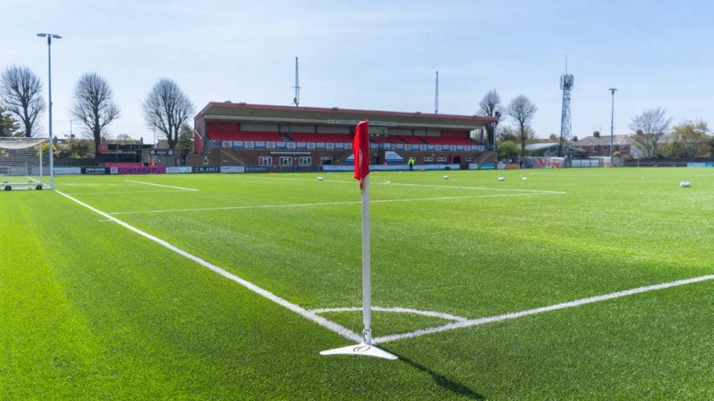 The pitch at Worthing FC's ground, viewed from the corner flag across the turf and towards the main stand.