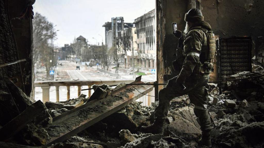 A Russian soldier takes a photo on his phone inside Mariupol's destroyed theatre, April 2022