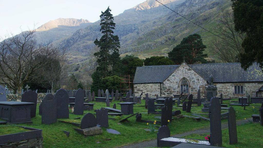 Mae Eglwys Sant Peris, Nant Peris, yng nghysgod Crib Goch