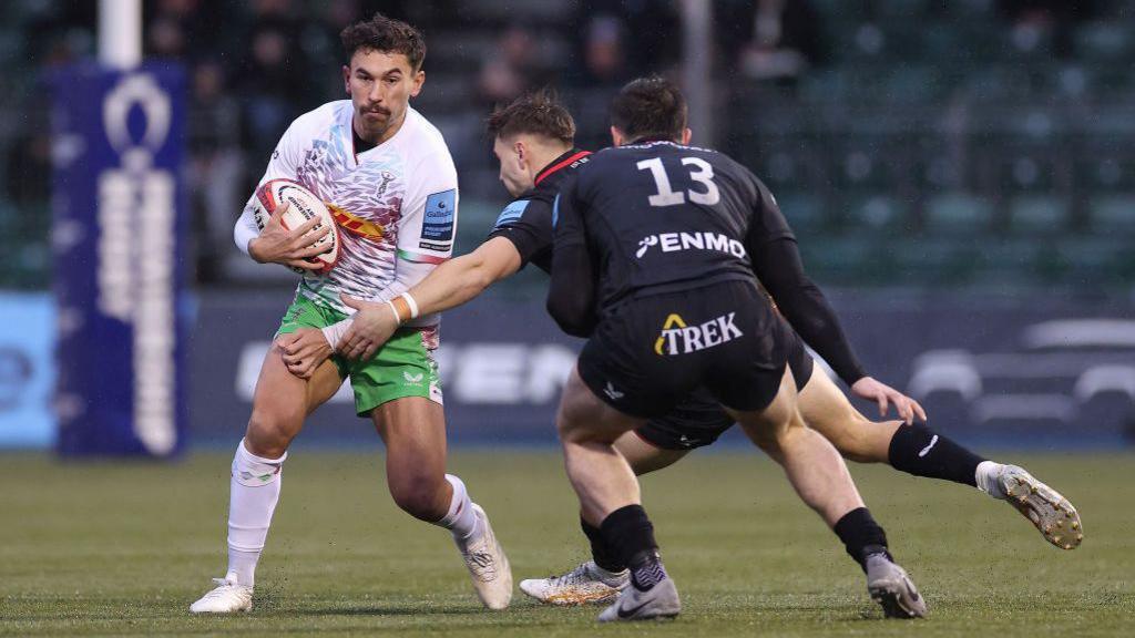 rugby player looks for a gap as he is tackled by two opponets 