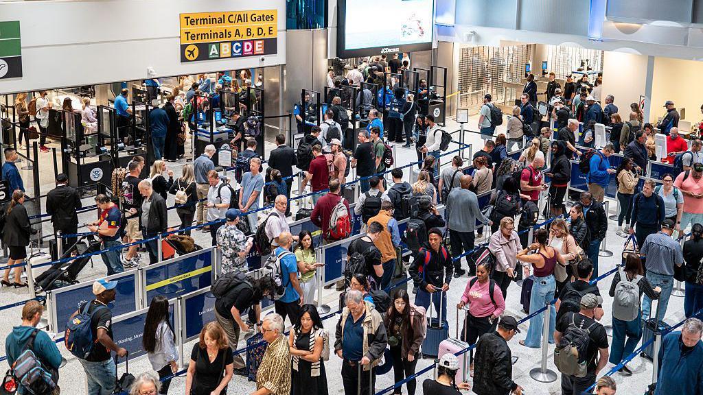 long line of people with suitcases waiting for a security checkpoint in airport