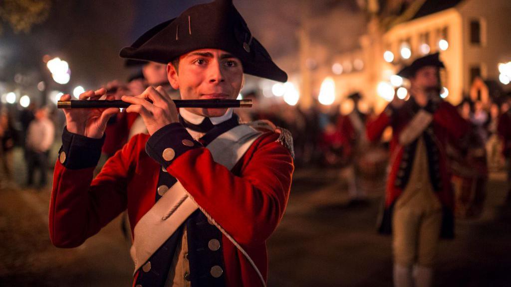 A man in historic military uniform plays the fife.