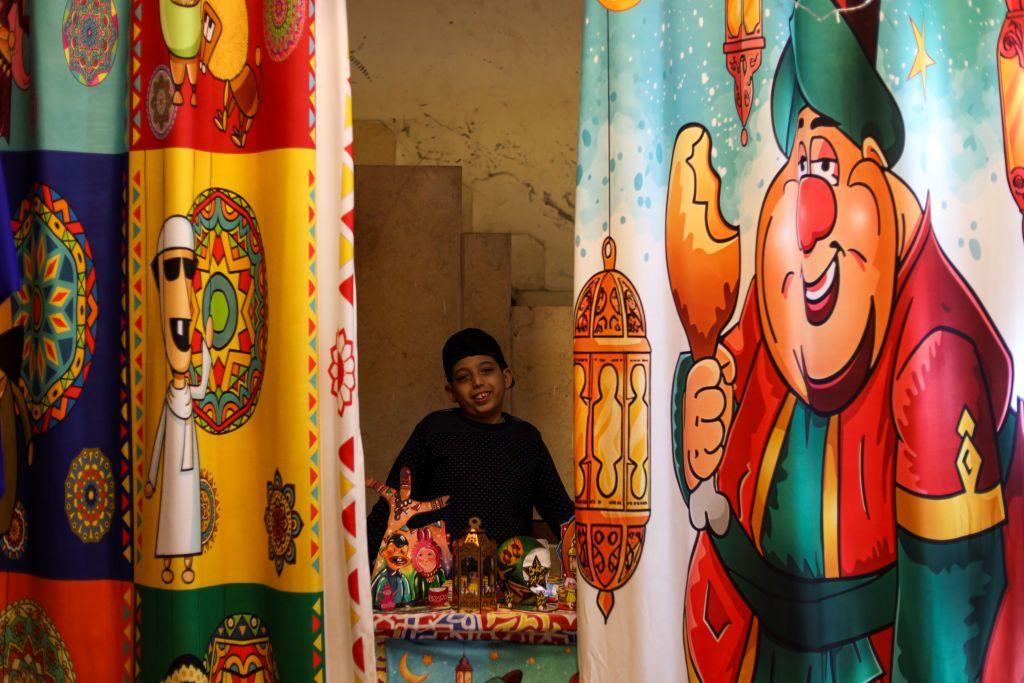 A boy stands next to lanterns and smiles. Either side of him are curtains printed with colourful cartoons.