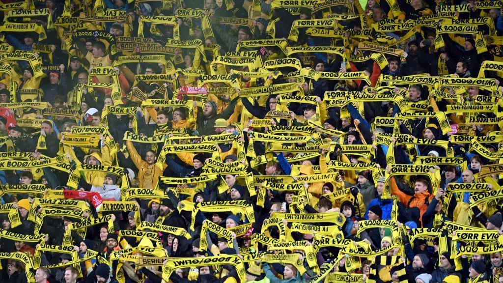Bodo/Glimt fans in the stands with yellow scarfs.