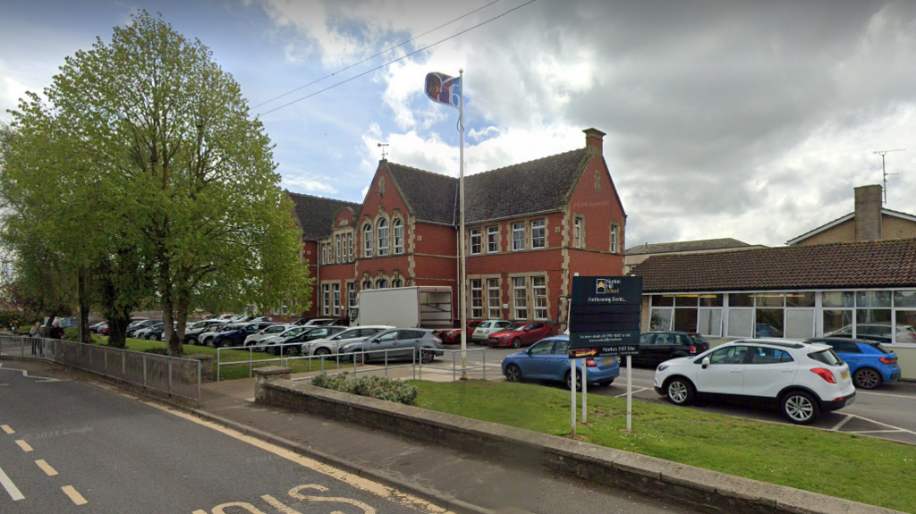 A school building with cars parked outside, and a bus stop