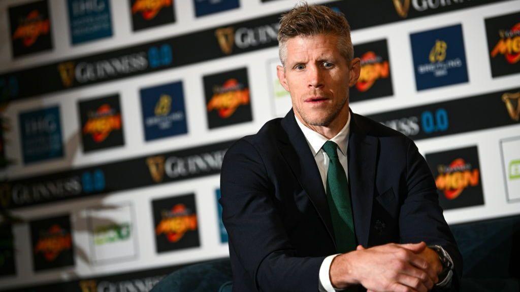 Llun o Simon Easterby yn gwisgo siwt a thei gwyrdd. Bwrdd llawn hysbysebion yn y cefndir gan gynnwys Guinness.