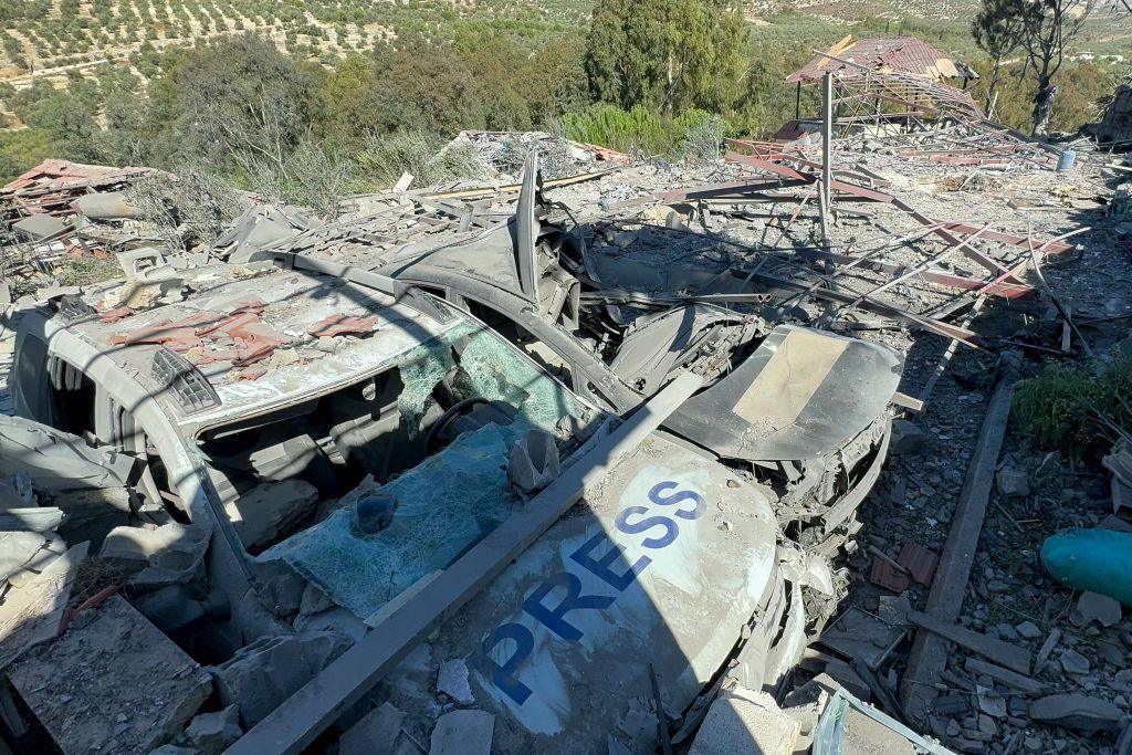 Two heavily damaged SUVs, with shattered windows and crumpled frames. One has the world word "press" written on its bonnet. Rubble and twisted metal is piled on top of them and around them.