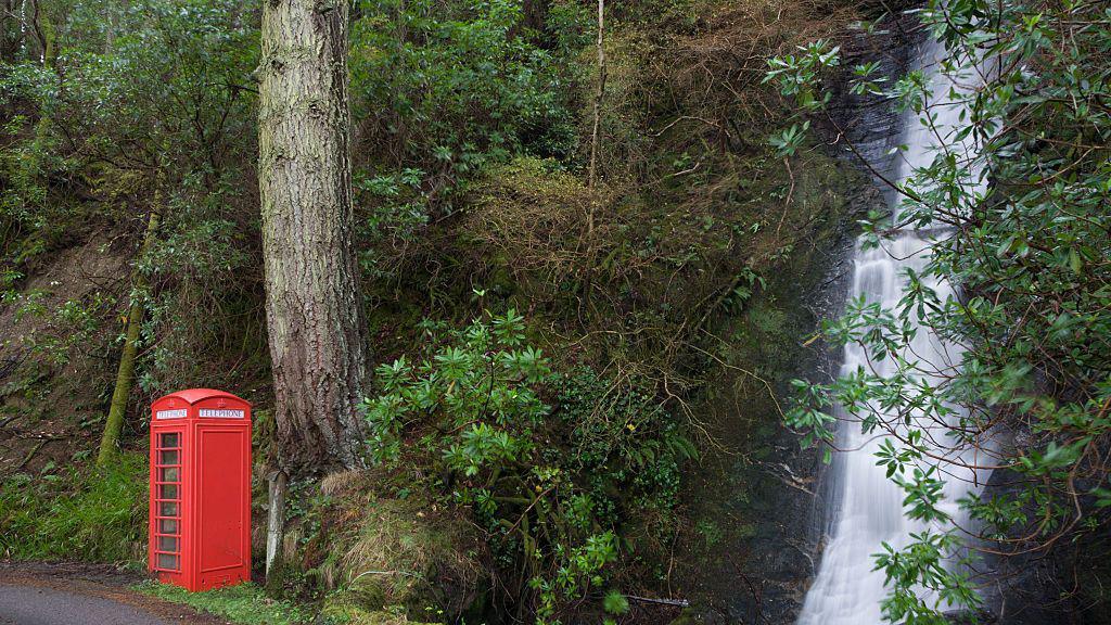 A bright red phone box, sitting next to a waterfall