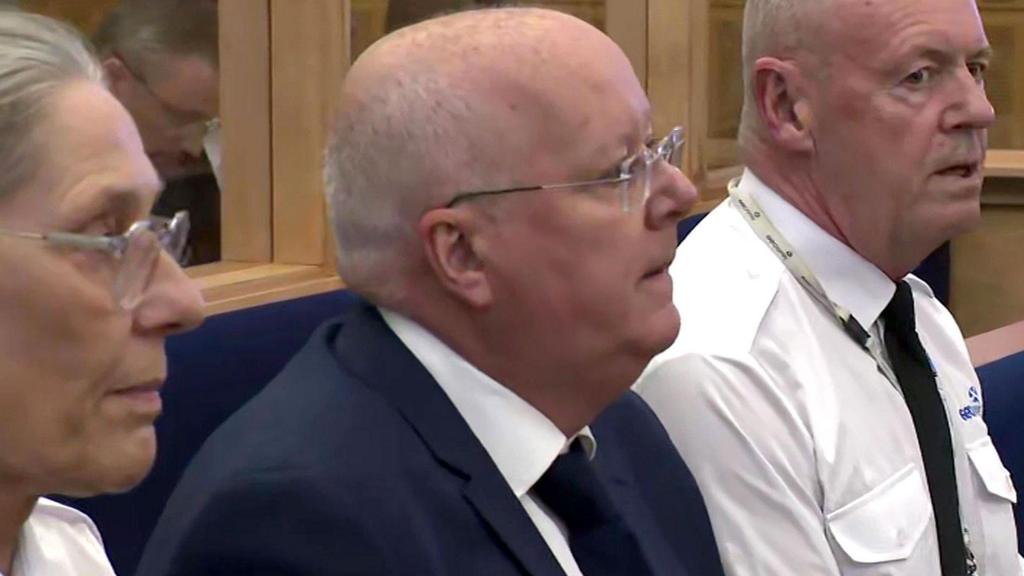 Peter Murrell sits between two guards inside the courtroom in Edinburgh
