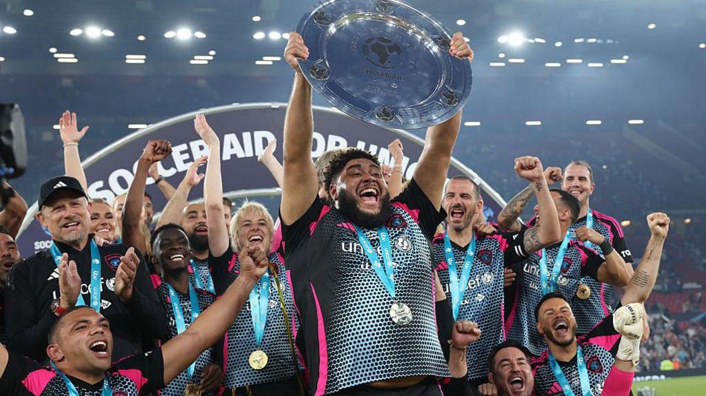 Big Zuu lifts the Soccer Aid trophy as World XI players celebrate their victory in 2025.