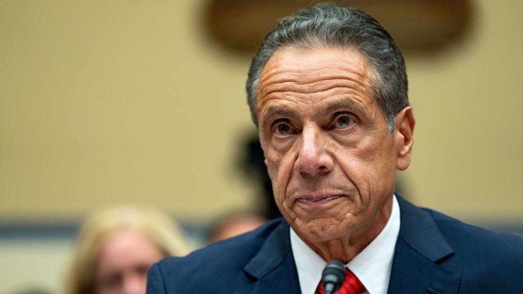 Andrew Cuomo sits wearing a blue suit 