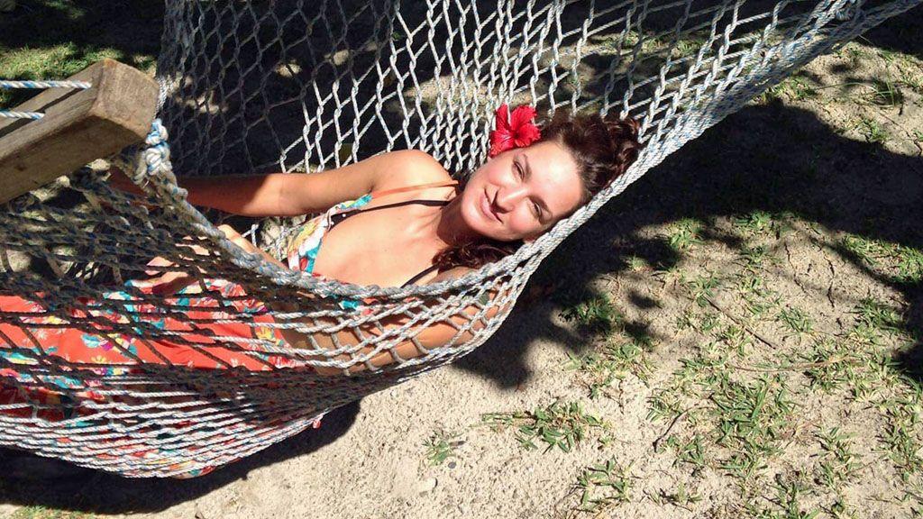 Picture of Sarm smiling from a hammock. She is wearing a patterned dress and has a red flower tucked behind her ear.
