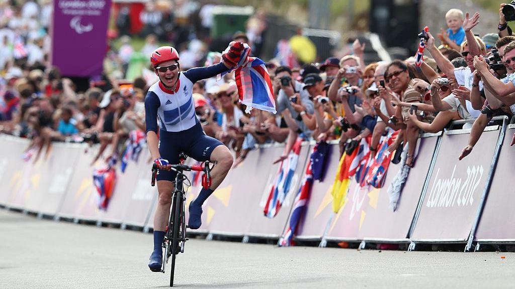 Sarah Storey celebrates crossing the line on her bike during London 2012 with fans celebrating behind the barrier