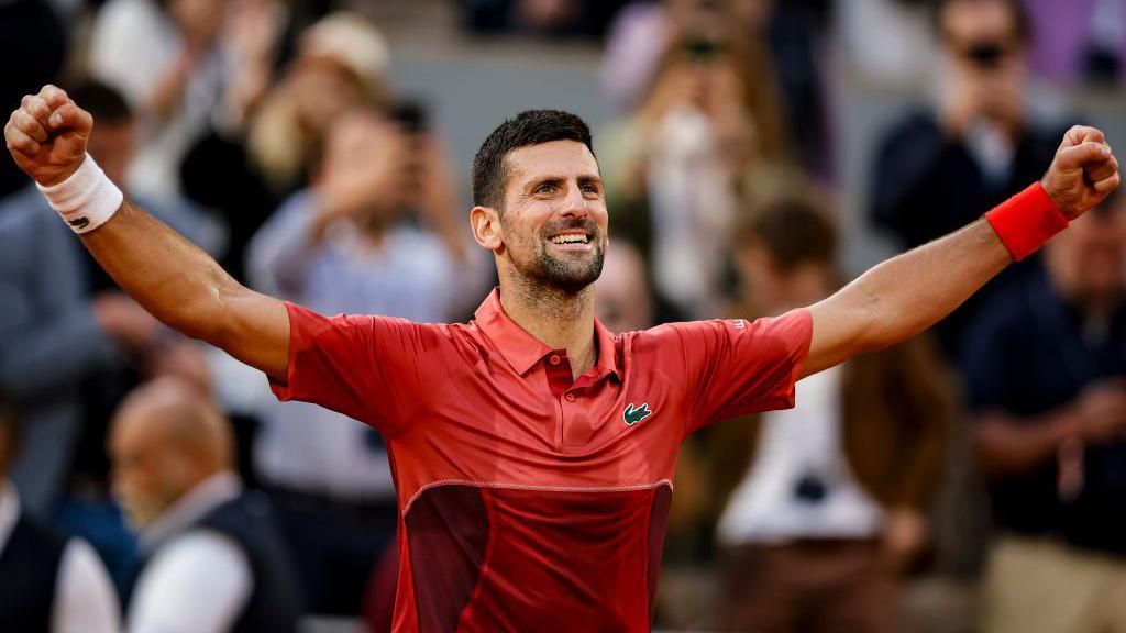 Novak Djokovic celebrates with arms up to the side and a broad smile