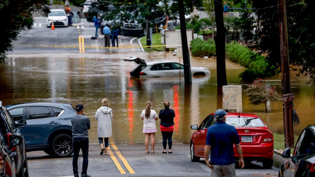 People look at car submerged in water in Peachtree Creek