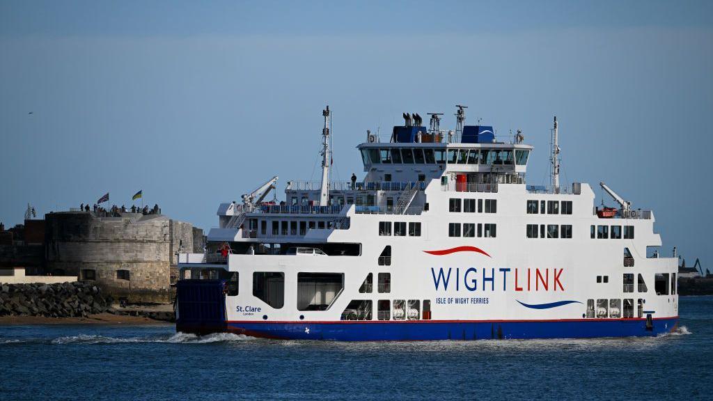 A blue and white ferry with the Wightlink logo on it, sailing out of a harbour on a bright sunny day.