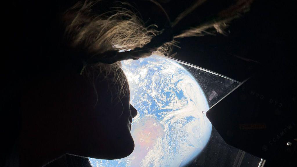 Christina Koch peering out of one of the Orion spacecraft's main cabin windows.
