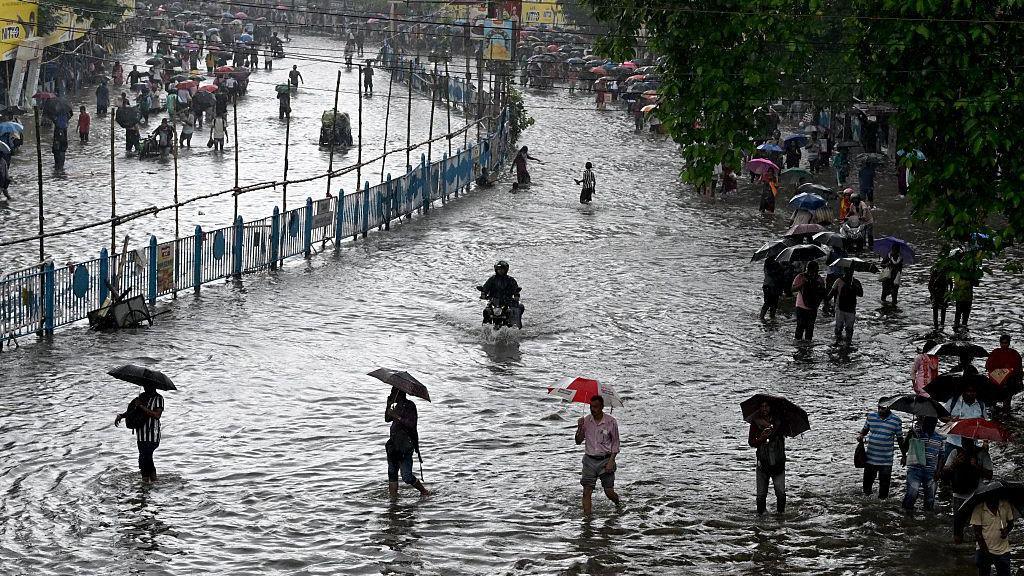 People wading through knee-deep waters on a flooded road in India's Kolkata city