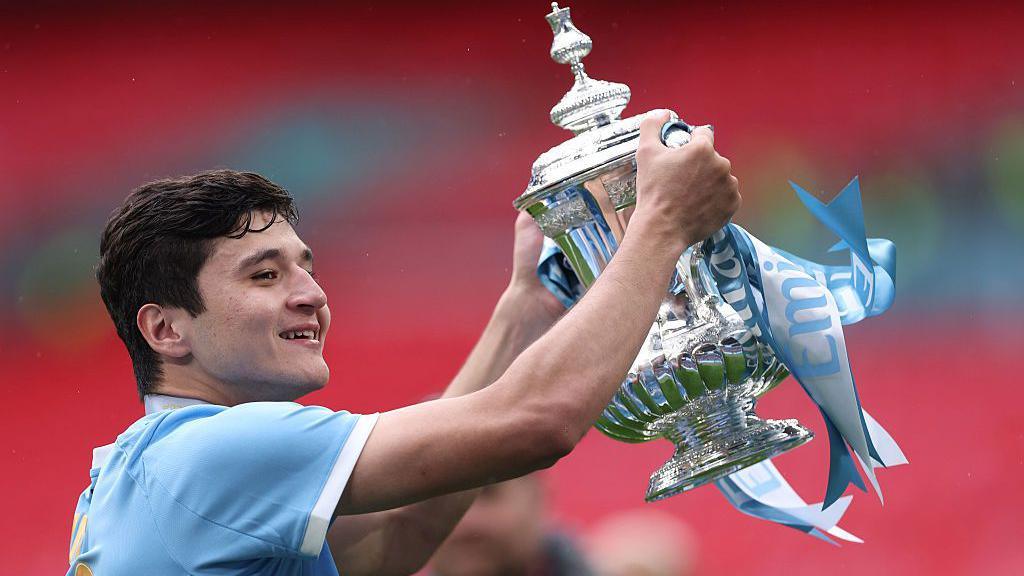 Abdukodir Khusanov smiling and lifting the FA Cup trophy for Manchester City