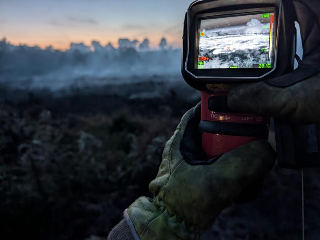 Firefighter holds a thermal camera looking for hotspots in wildfire